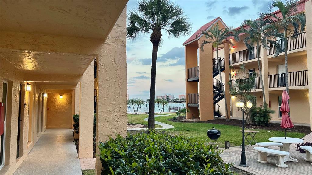 An exterior view shows a walkway, a courtyard with palm trees, and a waterfront building — 8931 BLIND PASS ROAD UNIT 158, ST PETE BEACH, FL
