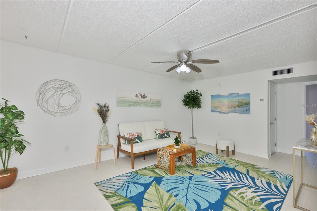 A living room features white walls, tile flooring, a tropical rug, and a ceiling fan — 8931 BLIND PASS ROAD UNIT 158, ST PETE BEACH, FL