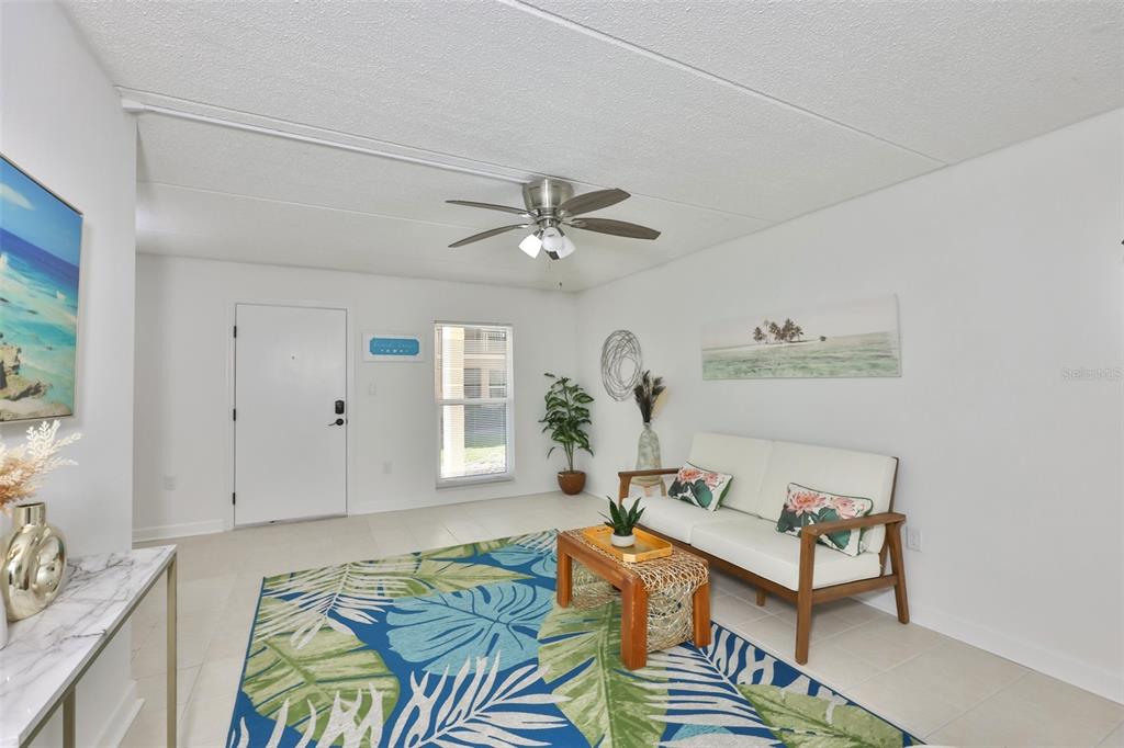 A living room features a tropical rug, a white sofa, and a ceiling fan — 8931 BLIND PASS ROAD UNIT 158, ST PETE BEACH, FL