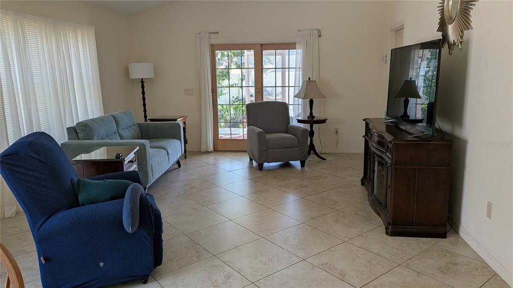 A living room features tile flooring, a blue sofa, a recliner, and a television console — 1231 ESTILL AVENUE, THE VILLAGES, FL