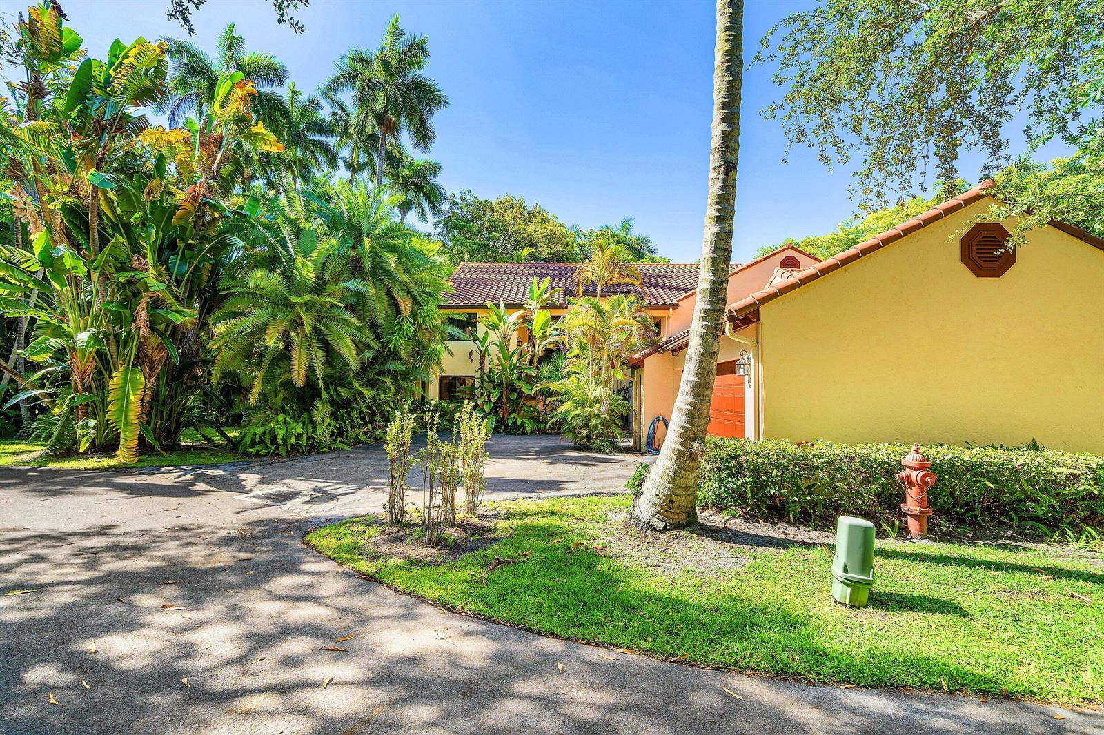 A yellow house with a tile roof and palm trees sits behind a paved driveway — 16 Via Lago, Boynton Beach FL 33435, BOYNTON BEACH, FL