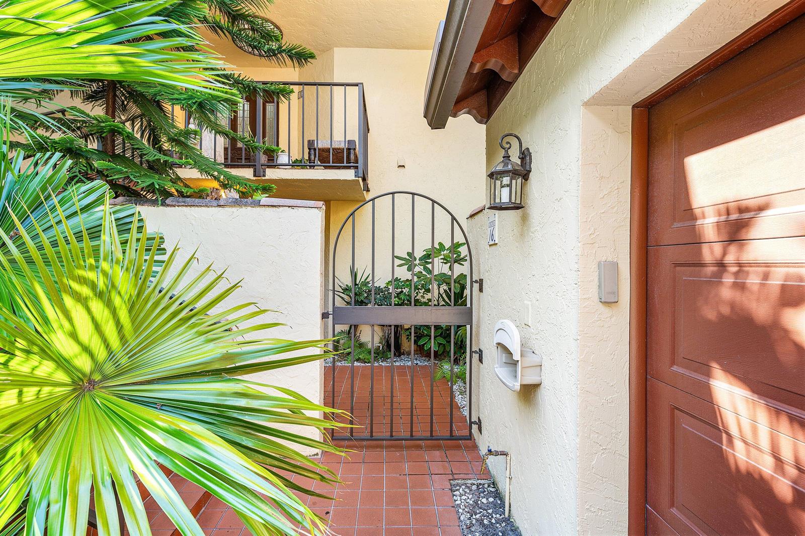 A tiled entryway features a metal gate, a wall-mounted lantern, and a brown garage door — 16 Via Lago, Boynton Beach FL 33435, BOYNTON BEACH, FL