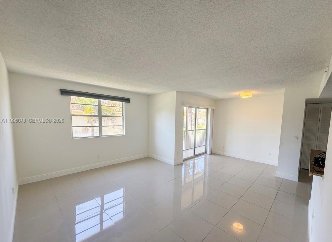 An open-concept living area features light-colored tile flooring, white walls, and a pass-through kitchen — 1253 SW 46th Ave # 1608, Pompano Beach FL 33069, POMPANO BEACH, FL