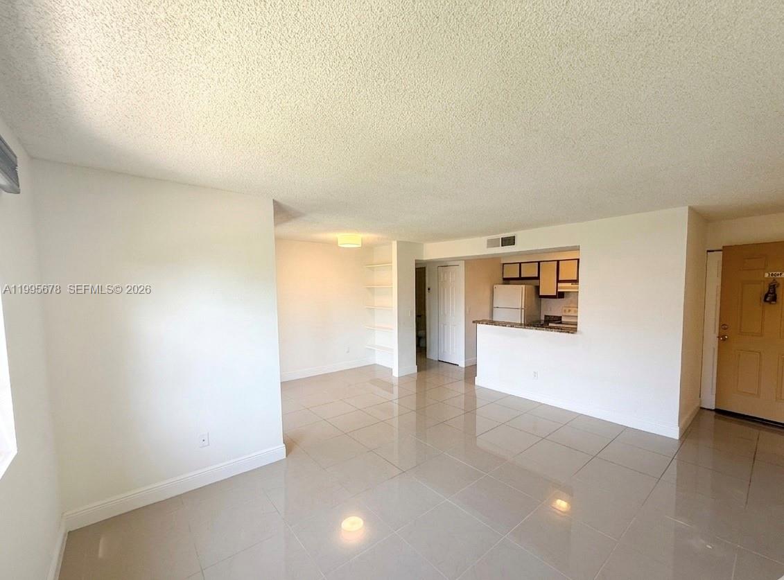 This living room features tile flooring, a built-in bookshelf, and an open kitchen area — 1253 SW 46th Ave # 1608, Pompano Beach FL 33069, POMPANO BEACH, FL