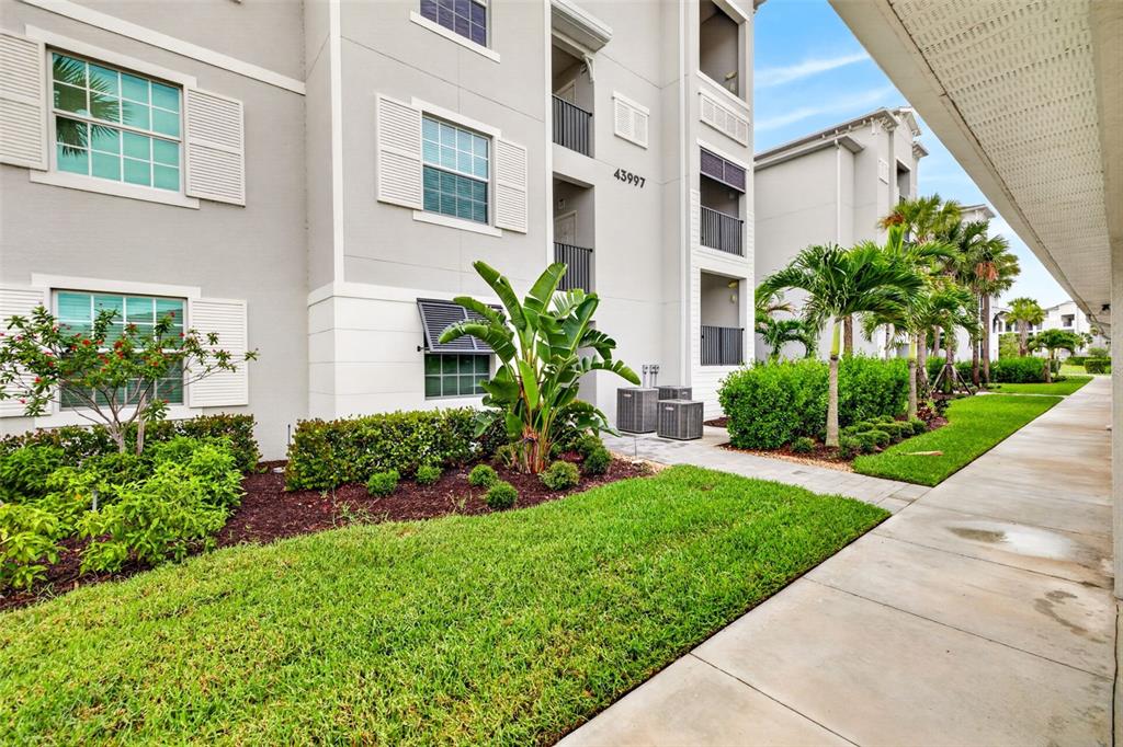 A multi-story apartment building exterior features a sidewalk, green lawn, and tropical landscaping — 43997 BOARDWALK LOOP UNIT 1841, PUNTA GORDA, FL