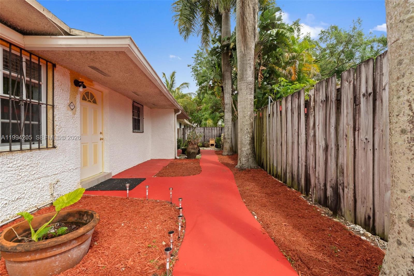 A red concrete walkway leads along the side of a house past a wooden fence — 3147 Mcdonald St, Miami FL 33133, MIAMI, FL