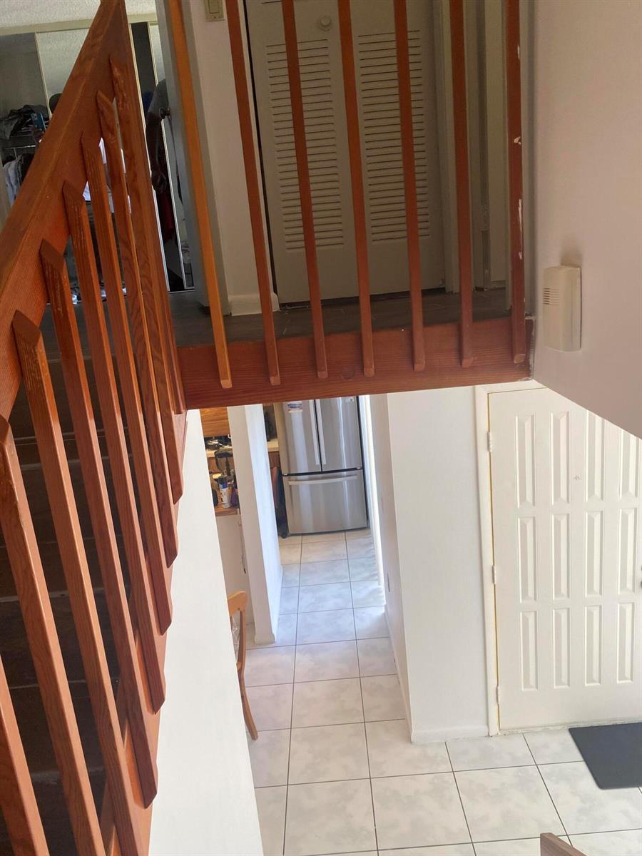 A view looking down a wooden staircase toward a tiled entryway and kitchen area — 3418 34th Way, West Palm Beach FL 33407, WEST PALM BEACH, FL