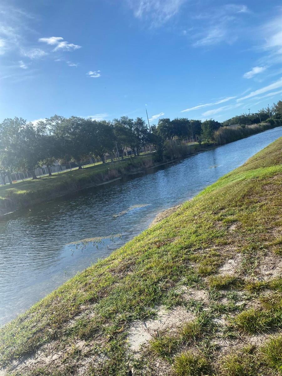 A narrow canal flows between grassy banks lined with trees under a blue sky — 3418 34th Way, West Palm Beach FL 33407, WEST PALM BEACH, FL