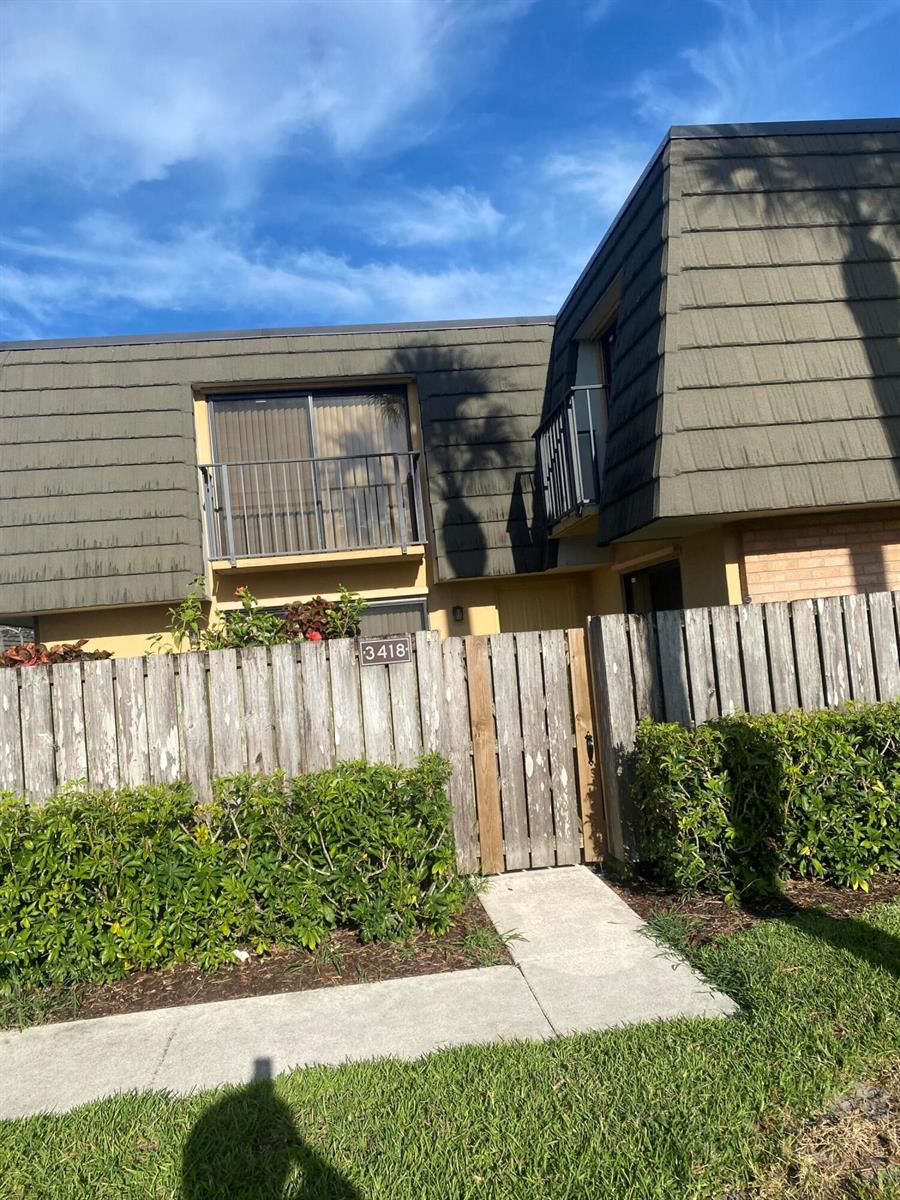 A two-story townhouse exterior features a wooden fence, a small balcony, and a concrete walkway — 3418 34th Way, West Palm Beach FL 33407, WEST PALM BEACH, FL