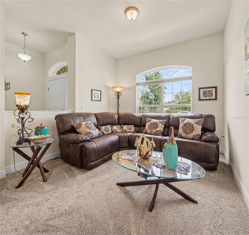 A living room features a brown leather sectional sofa, a glass coffee table, and carpeted flooring — 503 W LEAH COURT, FRUITLAND PARK, FL