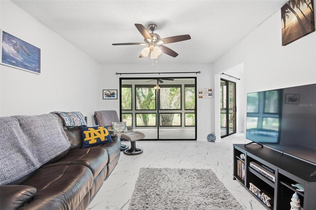 A living room features a brown leather sofa, a television, and a large sliding glass door — 20 MASTERS COURT UNIT 20, PALM COAST, FL