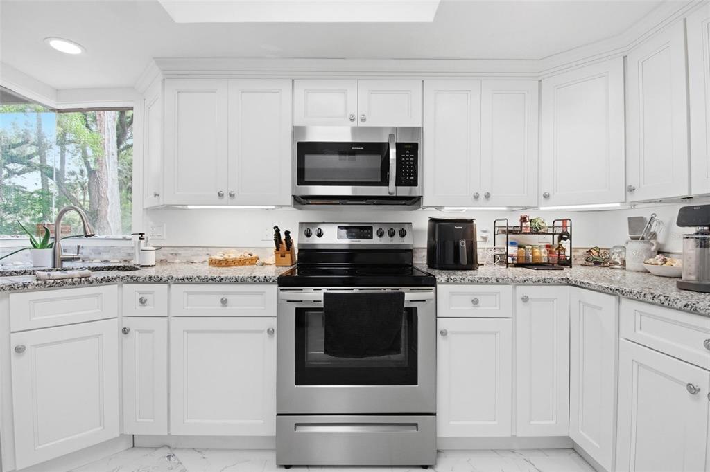 A kitchen features white cabinets, stainless steel appliances, granite countertops, and a window over the sink — 20 MASTERS COURT UNIT 20, PALM COAST, FL