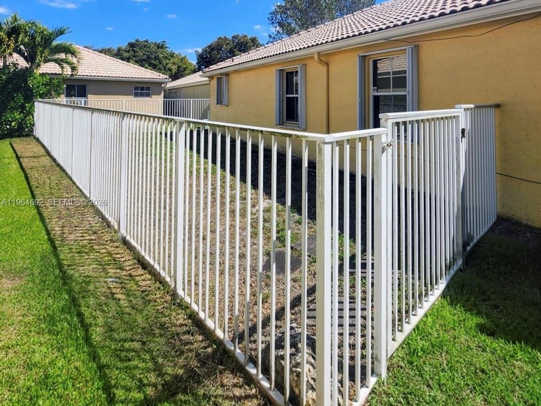 A white metal fence encloses a small yard area next to a yellow house — 4309 Pine Ridge Ct, Weston FL 33331, WESTON, FL