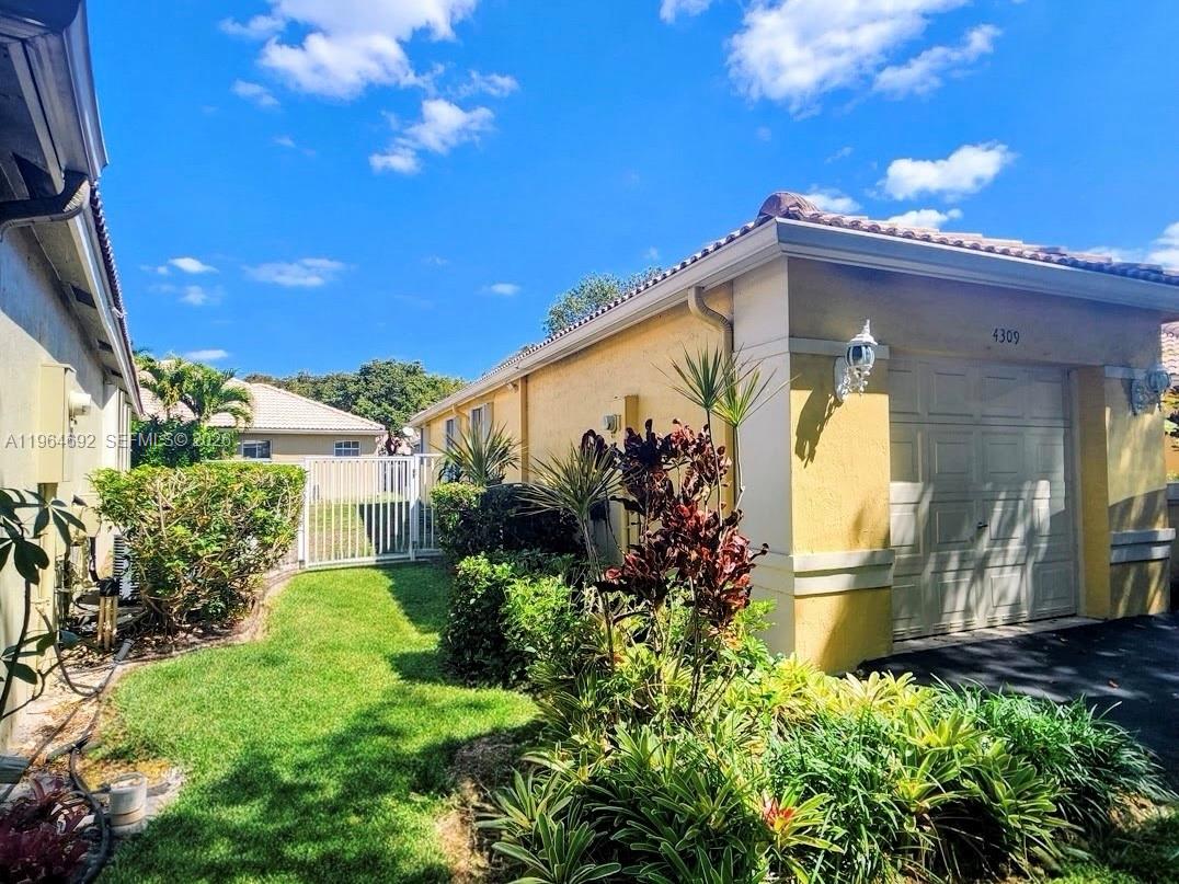 A yellow house exterior features a garage, a small lawn, and various tropical plants — 4309 Pine Ridge Ct, Weston FL 33331, WESTON, FL