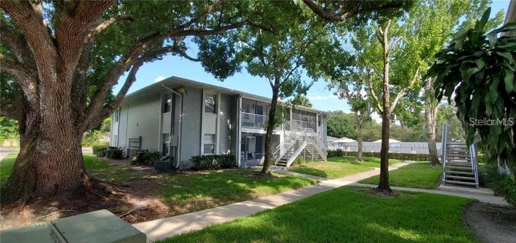 A two-story apartment building with exterior staircases sits on a grassy lawn with large trees — 700 E AIRPORT BOULEVARD UNIT A5, SANFORD, FL