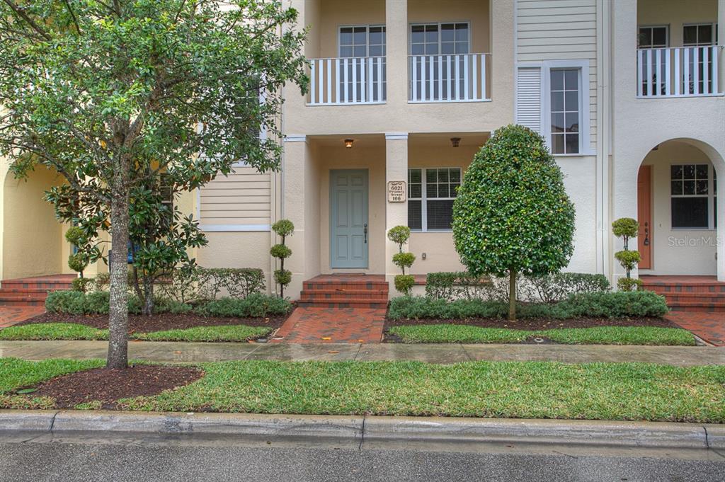 A multi-story townhouse exterior features a light blue front door, brick steps, and manicured landscaping — 6021 PRINTERY STREET UNIT 106, TAMPA, FL