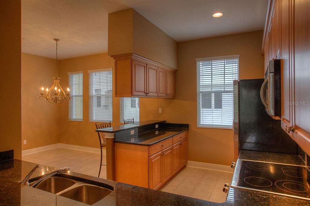 A kitchen with wood cabinets, granite countertops, and an adjacent dining area with a chandelier — 6021 PRINTERY STREET UNIT 106, TAMPA, FL
