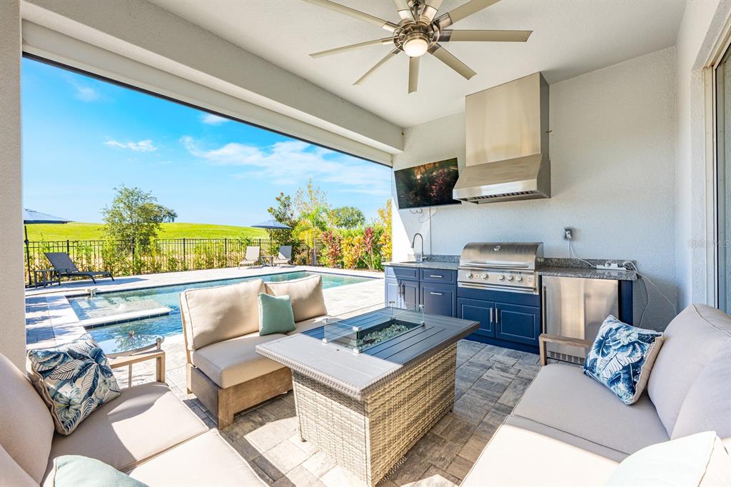 A covered outdoor patio features a kitchen, fire pit, seating area, and a swimming pool — 15714 VETTA DRIVE, BELLA COLLINA, FL