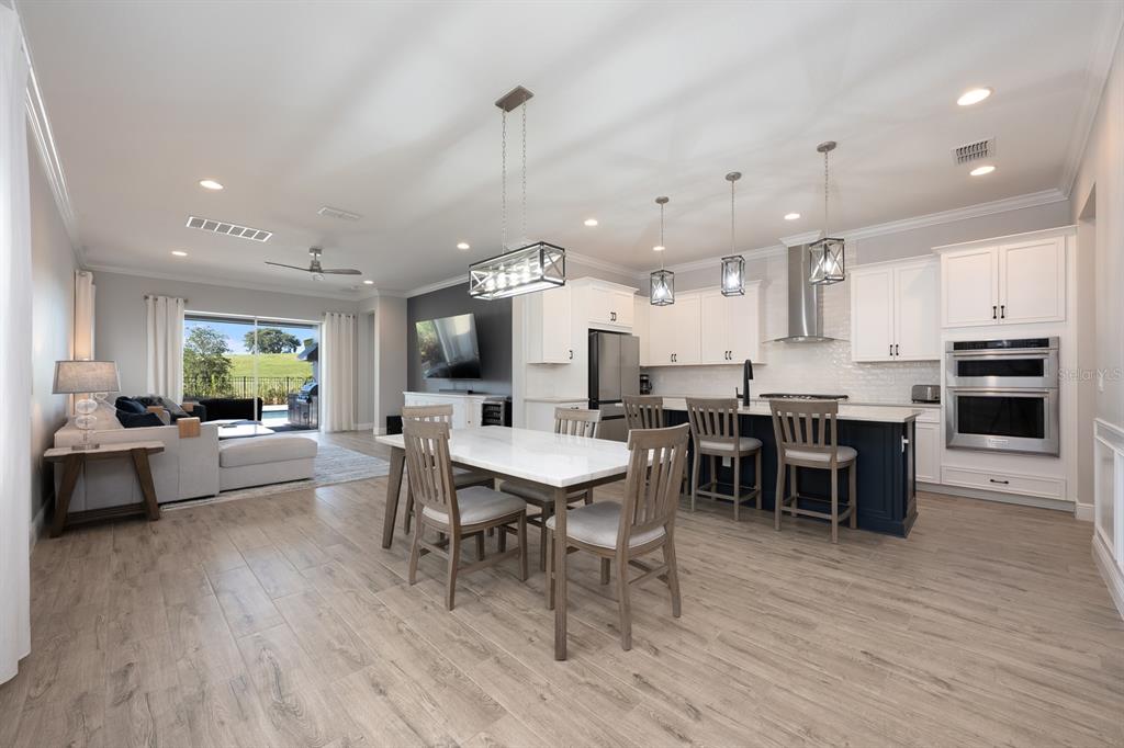 An open-concept kitchen and dining area features white cabinetry, a dark island, and wood-look flooring — 15714 VETTA DRIVE, BELLA COLLINA, FL