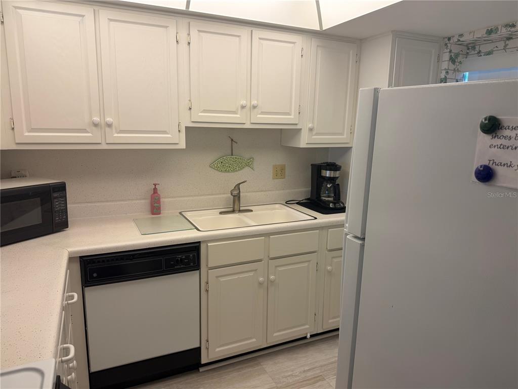 A kitchen features white cabinets, a double sink, a dishwasher, and a white refrigerator — 1400 TARPON CENTER DRIVE UNIT 202, VENICE, FL