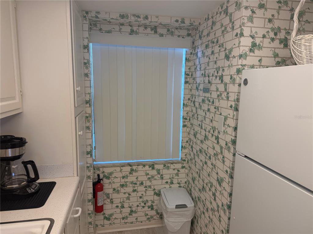 A kitchen corner features white cabinets, a white refrigerator, and ivy-patterned wallpaper — 1400 TARPON CENTER DRIVE UNIT 202, VENICE, FL