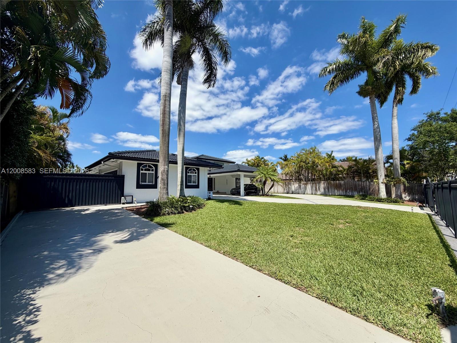 A white house with a black roof and trim sits behind a large lawn and palm trees — 13431 SW 32nd St, Miami FL 33175, MIAMI, FL