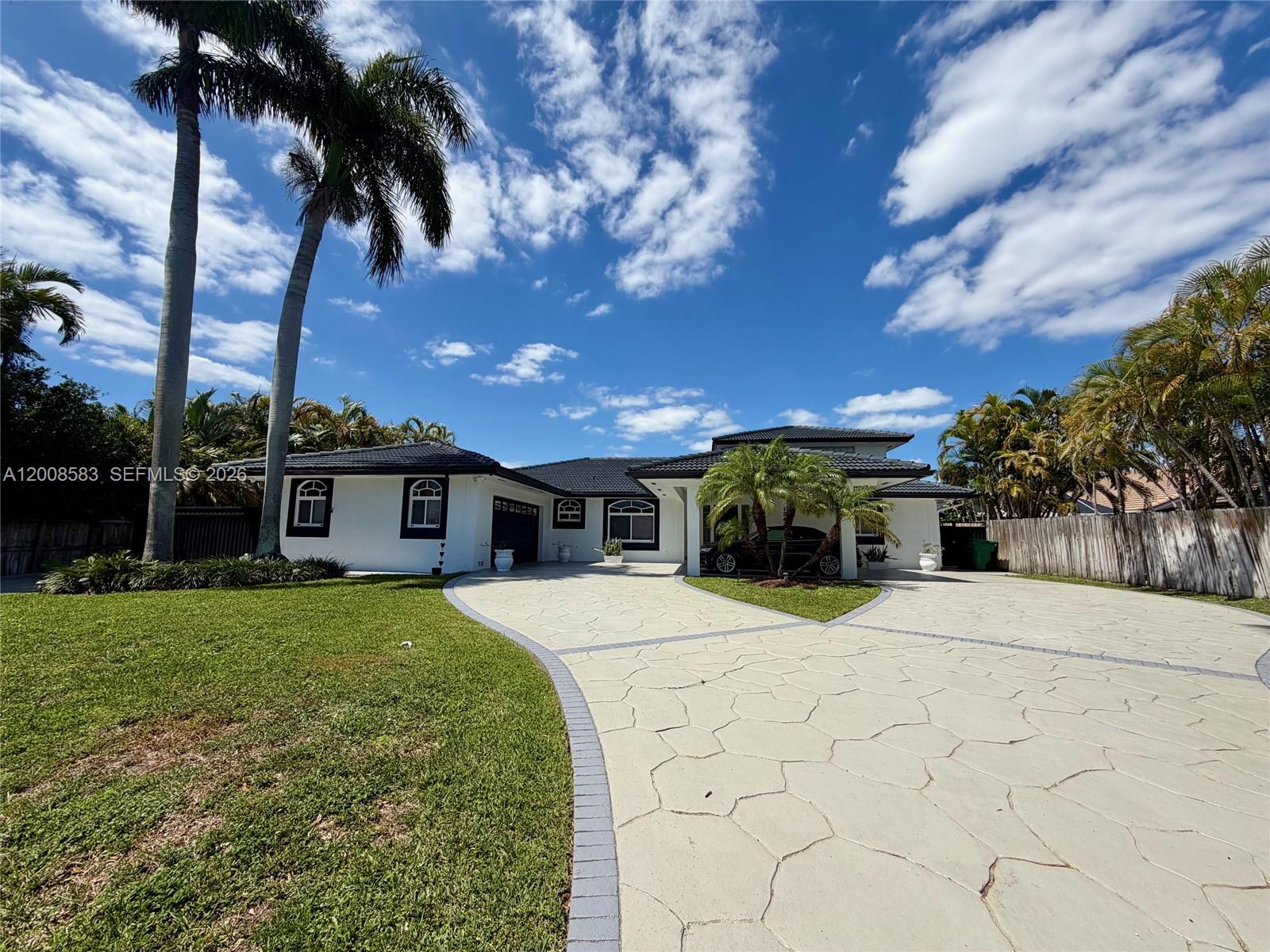A white single-story house with a patterned concrete driveway and palm trees under a blue sky — 13431 SW 32nd St, Miami FL 33175, MIAMI, FL