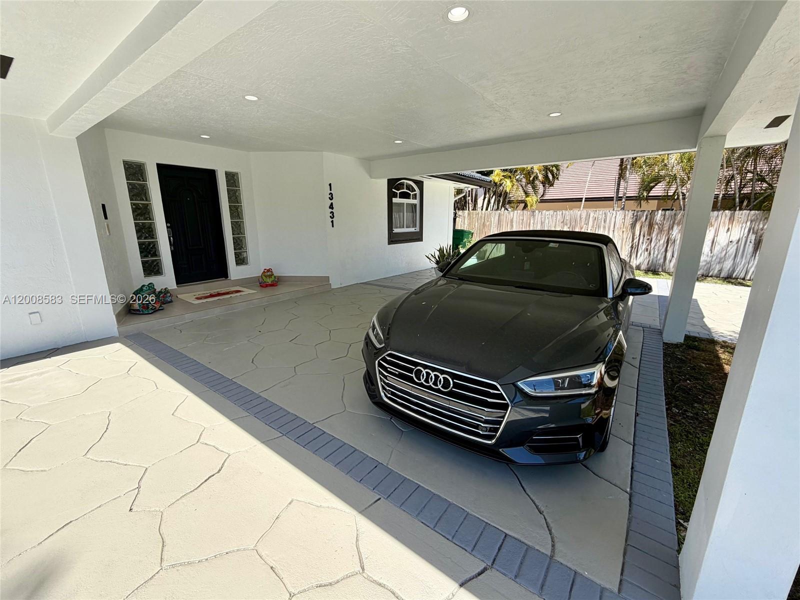 A dark car is parked under a covered carport in front of a white house — 13431 SW 32nd St, Miami FL 33175, MIAMI, FL