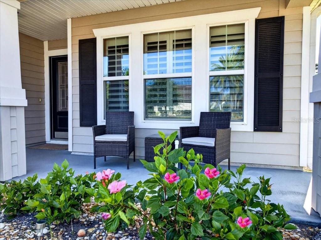 A covered front porch features two wicker chairs, a small table, and blooming hibiscus plants — 6 COUNTRY CLUB HARBOR CIRCLE, PALM COAST, FL