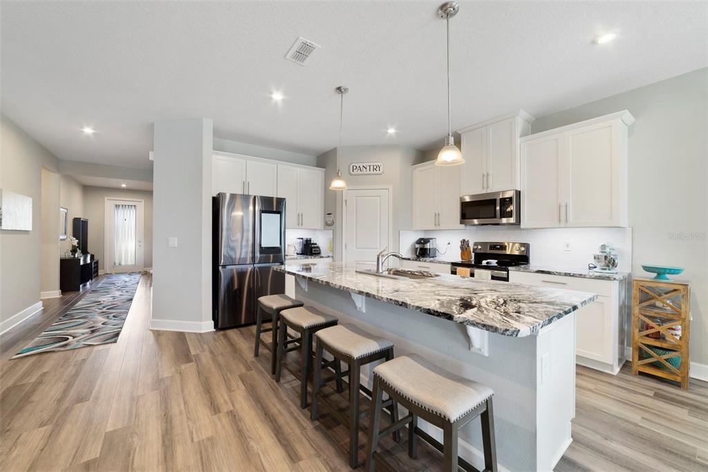 A modern kitchen features a granite-topped island, stainless steel appliances, and light-colored cabinetry — 173 LAVENNA AVENUE, ST CLOUD, FL