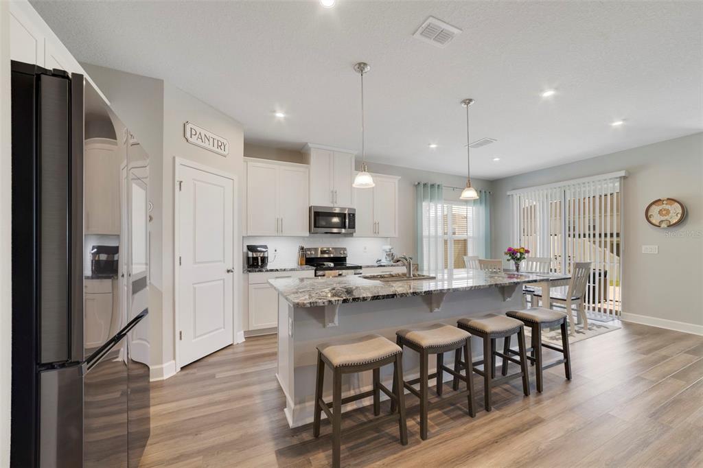 A modern kitchen features white cabinets, a granite island with four stools, and wood flooring — 173 LAVENNA AVENUE, ST CLOUD, FL