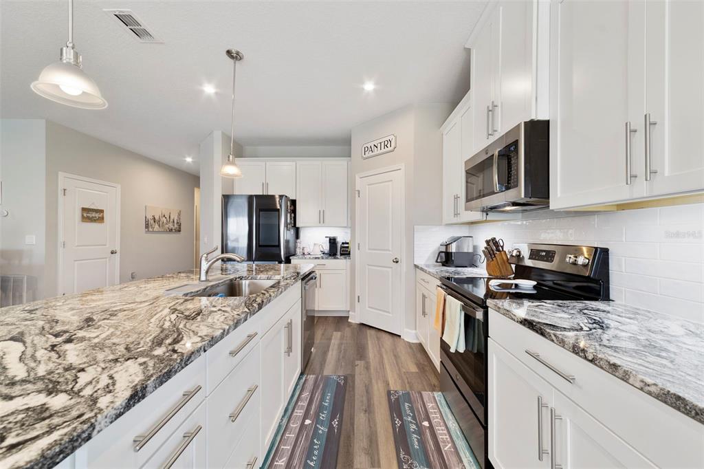 A modern kitchen features white cabinets, granite countertops, stainless steel appliances, and wood-look flooring — 173 LAVENNA AVENUE, ST CLOUD, FL