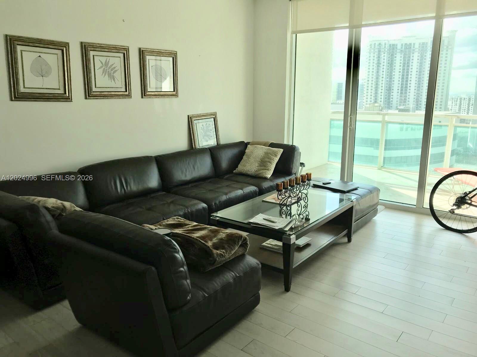 A living room features a dark leather sectional sofa, a glass coffee table, and balcony views — 950 Brickell Bay Dr # 2000, Miami FL 33131, MIAMI, FL