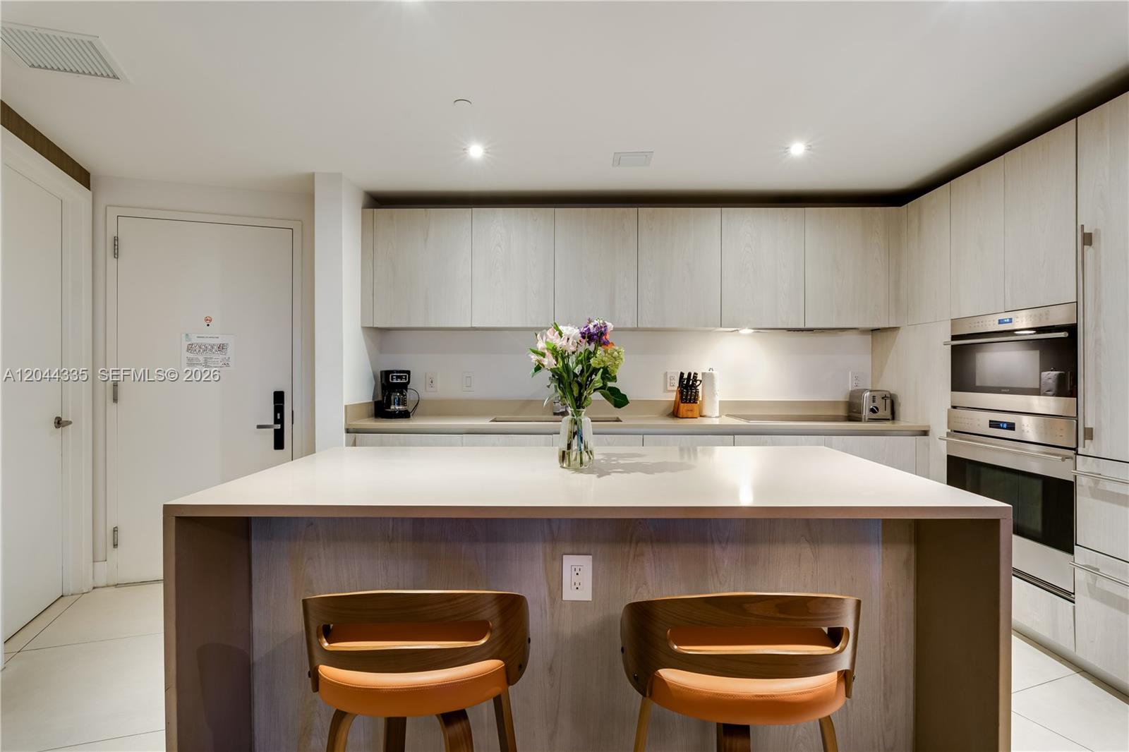 A modern kitchen features light wood cabinetry, a central island with two stools, and stainless appliances — 4111 S Ocean Dr # 1405, Hollywood FL 33019, HOLLYWOOD, FL