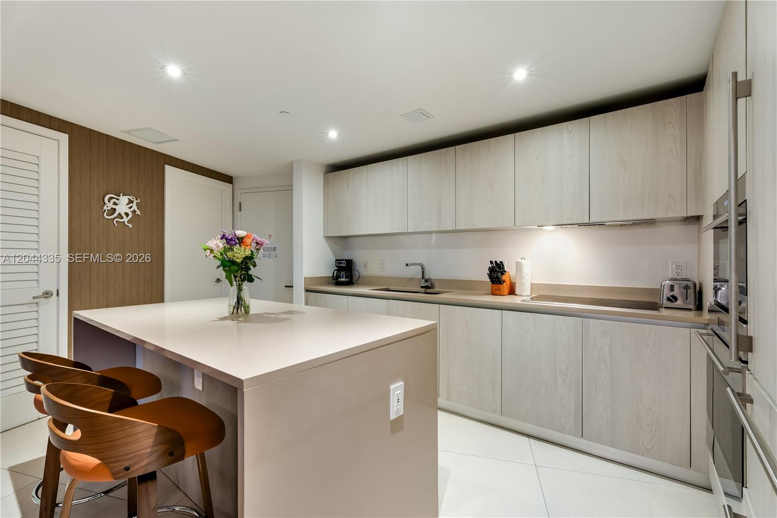 A modern kitchen features light wood cabinetry, a central island with bar stools, and countertops — 4111 S Ocean Dr # 1405, Hollywood FL 33019, HOLLYWOOD, FL