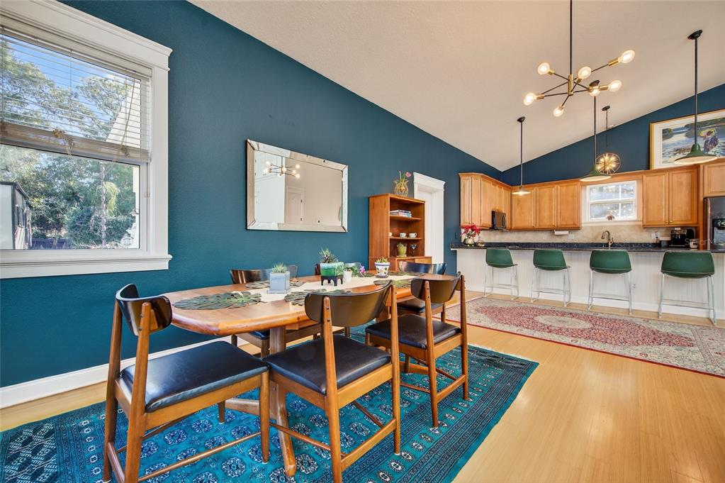 A dining area with a wooden table and chairs sits before a kitchen with bar seating — 615 ART CENTER AVENUE, NEW SMYRNA BEACH, FL