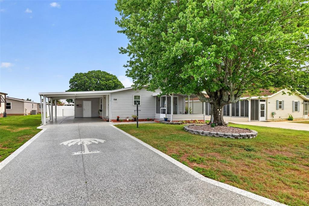 A single-story house with a carport, a painted driveway, and a large tree in front — 728 PRADO DRIVE, LADY LAKE, FL