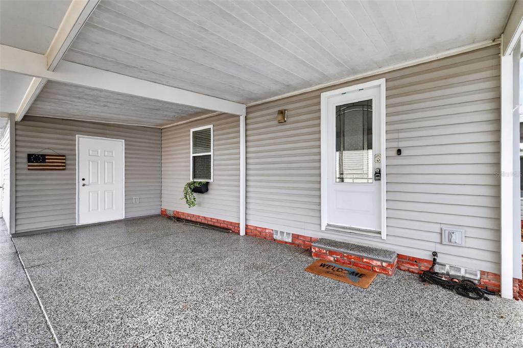 A covered concrete patio features light gray siding, two white doors, and brick accents — 728 PRADO DRIVE, LADY LAKE, FL