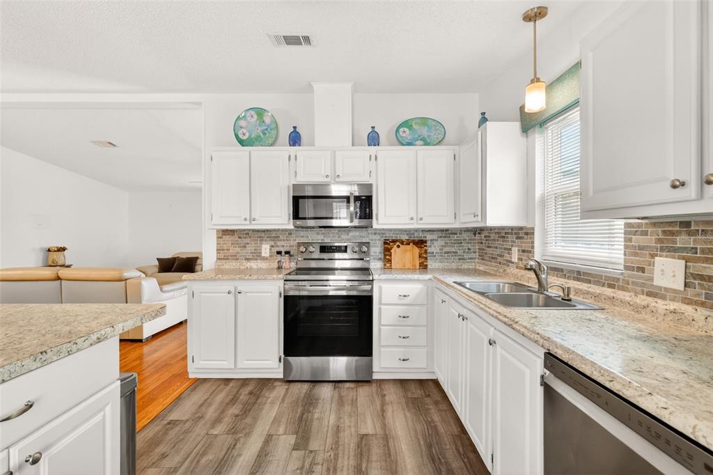 A kitchen with white cabinets, stainless steel appliances, granite countertops, and a tiled backsplash — 728 PRADO DRIVE, LADY LAKE, FL