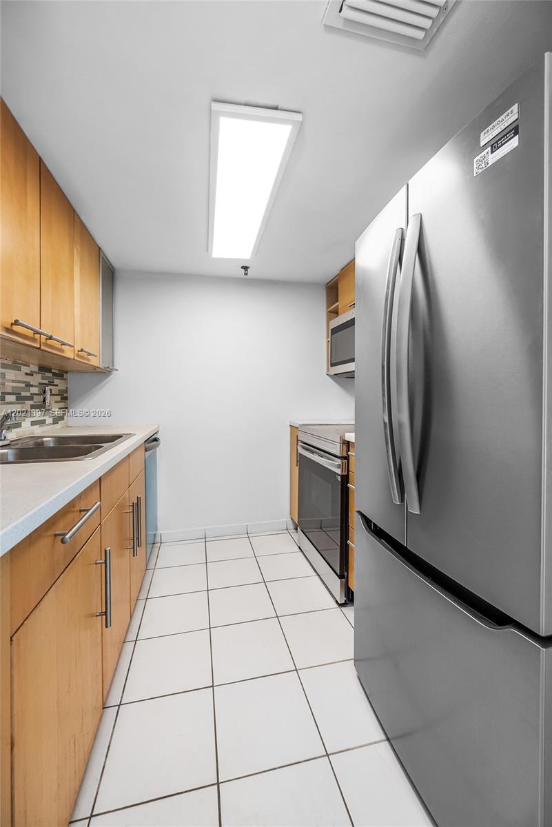 A galley kitchen features light wood cabinets, stainless steel appliances, and white tile flooring — 1010 NW 11th St # 507, Miami FL 33136, MIAMI, FL