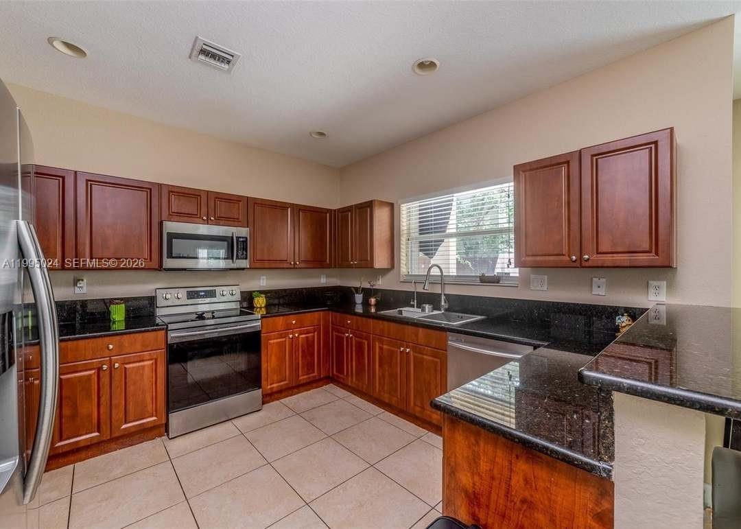 A kitchen features dark wood cabinets, black granite countertops, and light-colored tile flooring — 385 NE 36th Ave Rd, Homestead FL 33033, HOMESTEAD, FL