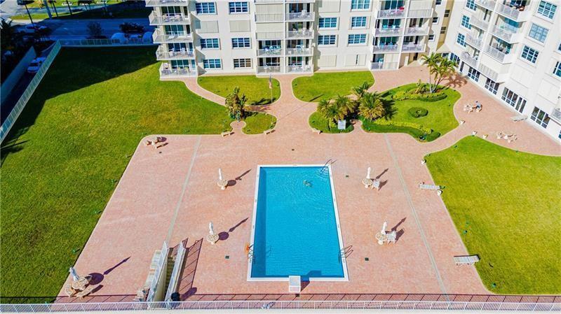 An aerial view shows a rectangular swimming pool surrounded by a paved deck and lawns — 750 N Ocean Boulevard # 1704, Pompano Beach FL 33062, POMPANO BEACH, FL
