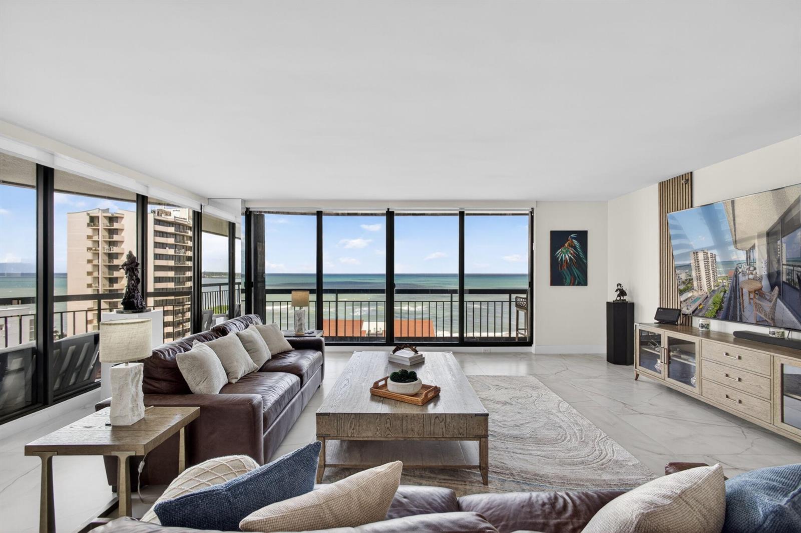 A living room with a leather sofa, wood coffee table, and floor-to-ceiling windows overlooking the ocean — 4100 N Ocean Drive # 1201, Singer Island FL 33404, SINGER ISLAND, FL