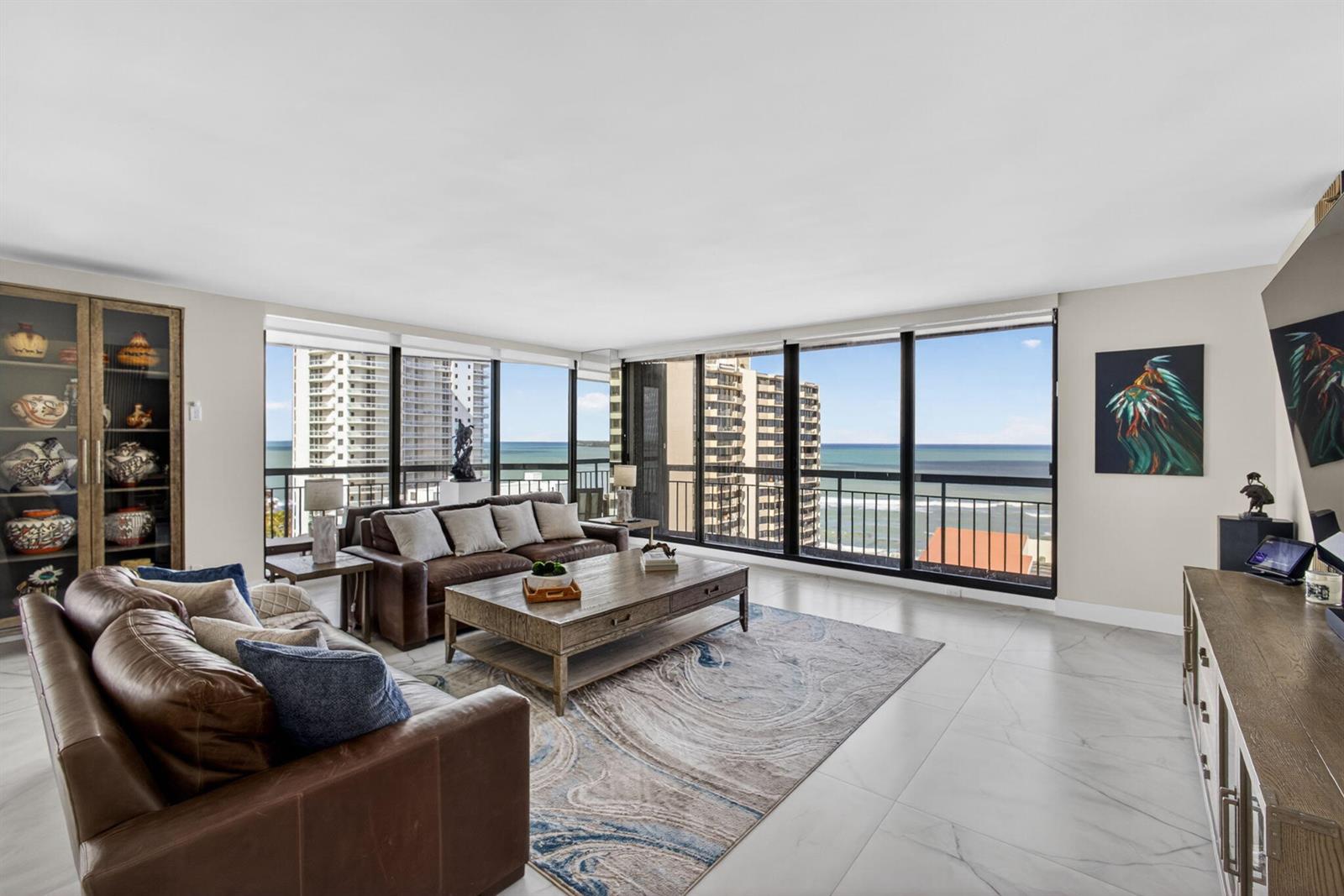 A living room features leather sofas, a coffee table, and floor-to-ceiling windows overlooking the ocean — 4100 N Ocean Drive # 1201, Singer Island FL 33404, SINGER ISLAND, FL