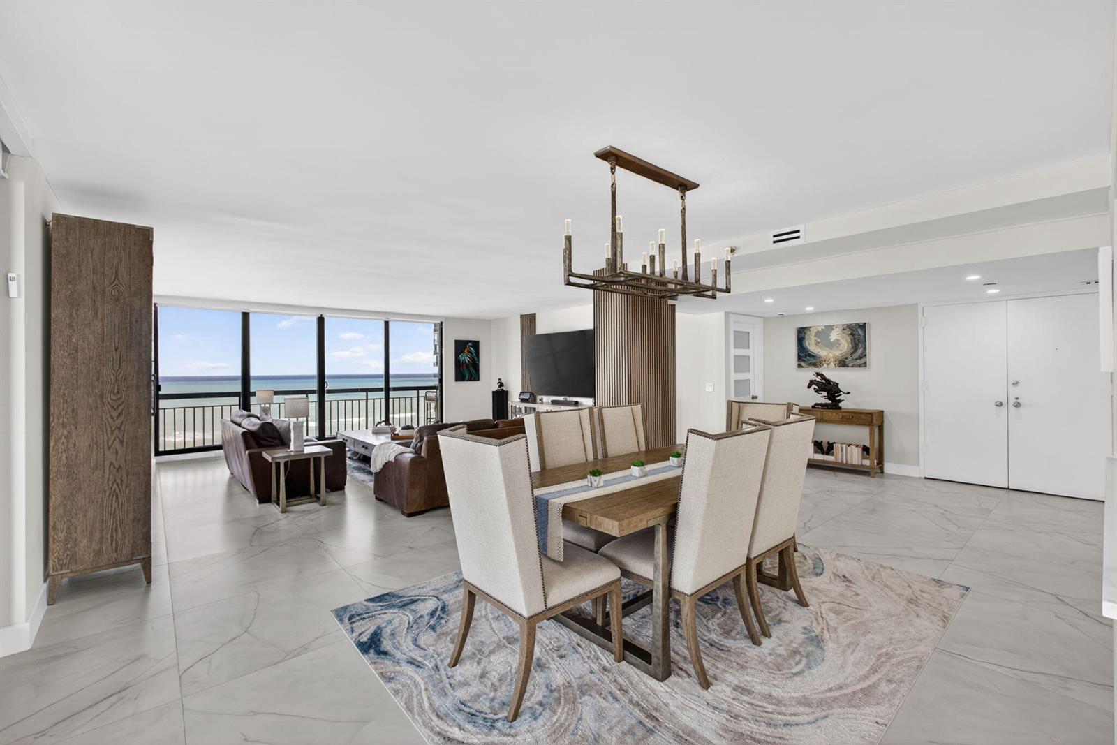 A dining area with a wooden table and chairs sits before a living room overlooking ocean — 4100 N Ocean Drive # 1201, Singer Island FL 33404, SINGER ISLAND, FL