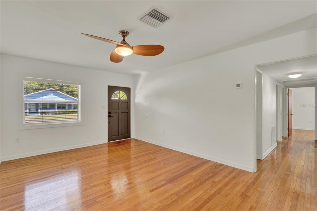 A living room with hardwood floors, a ceiling fan, a dark door, and a window — 3345 LILA DRIVE, ORLANDO, FL
