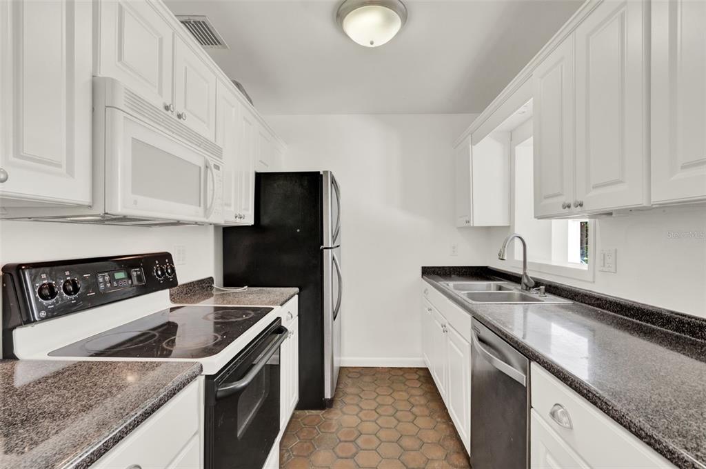 A galley kitchen features white cabinets, granite countertops, a black refrigerator, and hexagonal floor tiles — 3345 LILA DRIVE, ORLANDO, FL