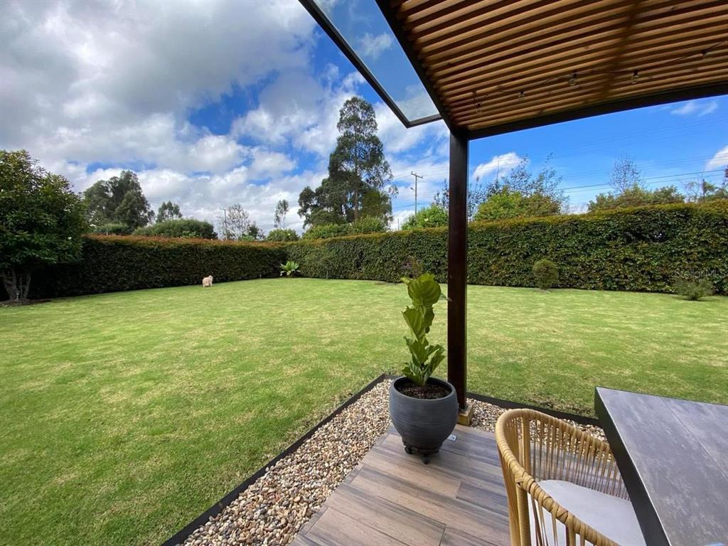 A patio with a pergola and potted plant overlooks a large, fenced-in grassy backyard — 47 CARRERA 47, BOGOTA, NY
