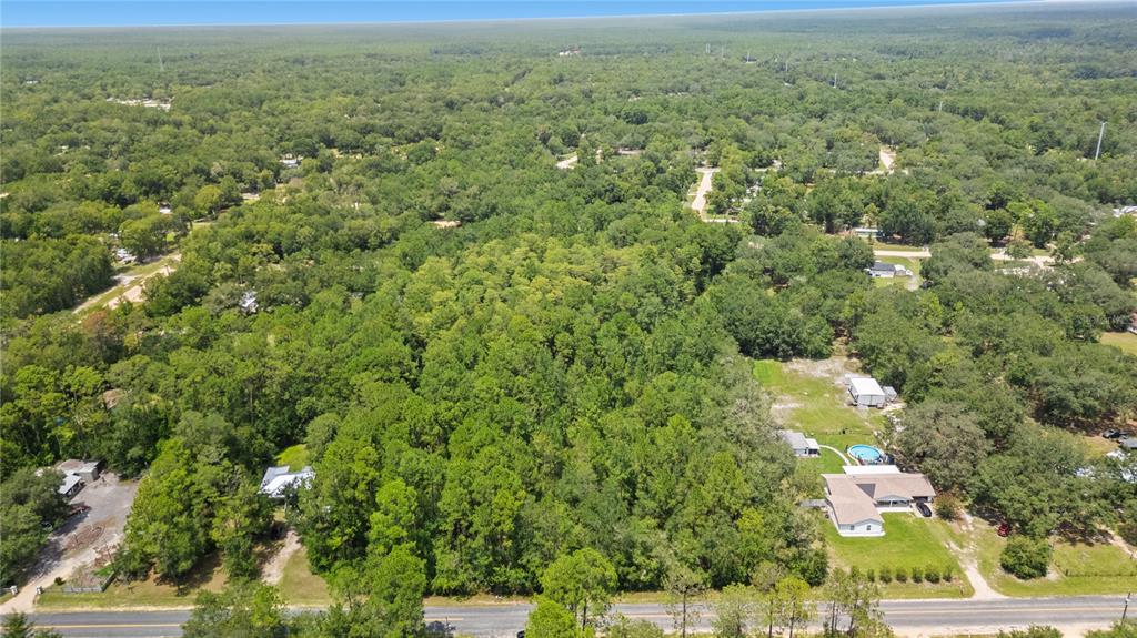An aerial view shows a wooded lot situated between several houses along a paved road — 150 SESAME STREET, MIDDLEBURG, FL
