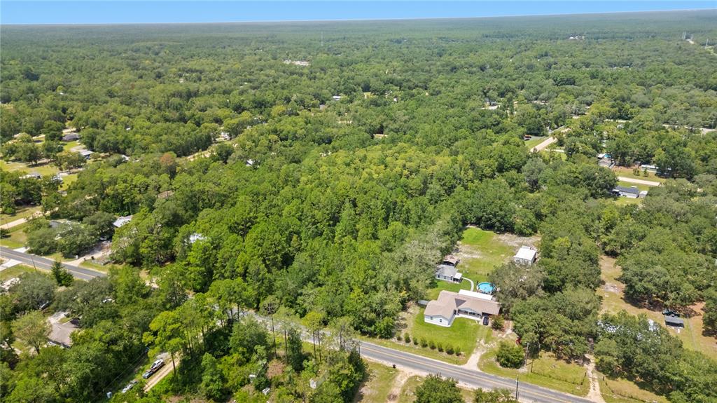 An aerial view shows a house with a pool surrounded by dense forest and roads — 150 SESAME STREET, MIDDLEBURG, FL